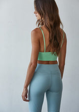 [Color: Mint Parfait] A back facing image of a brunette model wearing a basic lime green bralette cami with a slim stretchy fit and a v neckline.