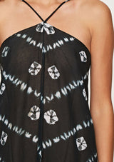 [Color: Black/Bone] A detail image of a brunette model wearing a white and black beach maxi dress with a halter neckline, strappy open back, and a flowy silhouette with tassel trim.