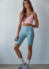 [Color: Pink] A front facing image of a brunette model wearing a basic light pink bralette cami with a slim stretchy fit and a v neckline.