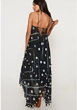 [Color: Black/Bone] A back facing image of a brunette model wearing a white and black beach maxi dress with a halter neckline, strappy open back, and a flowy silhouette with tassel trim.
