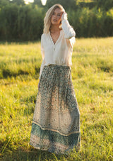 [Color: Taupe/Dusty Teal] A front facing image of a blonde model wearing a green teal floral bohemian skirt on a grassy field with an elastic drawstring waist and lace detail. A classic bohemian skirt for the fall season. 