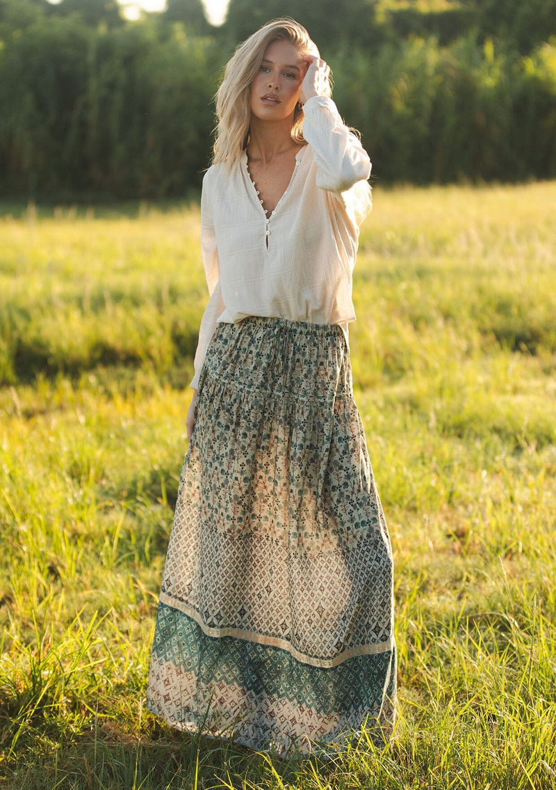 [Color: Taupe/Dusty Teal] A front facing image of a blonde model wearing a green teal floral bohemian skirt on a grassy field with an elastic drawstring waist and lace detail. A classic bohemian skirt for the fall season. 