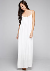 [Color: Off White] A front facing image of a brunette model wearing a white maxi dress with a relaxed fit, scoop neckline with crochet ball trim, and adjustable spaghetti straps. 