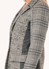 [Color: Cream/Black] A close up side facing image of a blonde model wearing a classic blazer in a grey patchwork plaid. With a button front, long sleeves, and side flap pockets. 