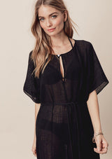 [Color: Black] A front facing image of a blonde model wearing a sheer black cotton midi dress with short sleeves, a front keyhole, and a braided waist belt. A stunning beach cover up for vacation. 