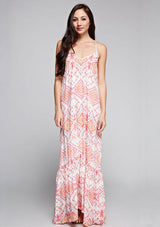 [Color: Coral/Rose/Multi] A front facing image of a brunette model wearing bohemian maxi dress with a pink geometric print, spaghetti straps, and a  racerback with tassel ties. 