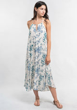 [Color: Ocean/Blue] A front facing image of a brunette model wearing a blue and white floral sleeveless halter maxi dress with a relaxed, flowy silhouette and tassel ties. Styled with brown strappy sandals. 