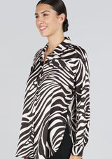 [Color: Black/Bone] A side facing image of a brunette model wearing a statement blouse with a black and white zebra print, button front, collared neck, and a relaxed, oversized fit.