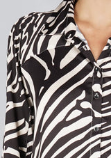[Color: Black/Bone] A detail image of a brunette model wearing a statement blouse with a black and white zebra print, button front, collared neck, and a relaxed, oversized fit.