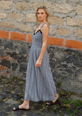 [Color: Black/White] A side facing image of a blonde model wearing a black and white gingham midi dress with a smocked bodice, tie shoulder straps, and side pockets. 