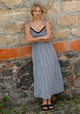 [Color: Black/White] A front facing image of a blonde model wearing a black and white gingham midi dress with a smocked bodice, tie shoulder straps, and side pockets. 
