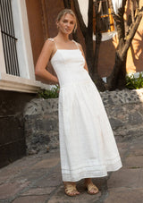 [Color: White] A front facing image of a blonde model outside wearing a white sheer plaid midi dress with tie shoulder straps, a drop waist, and side pockets. 