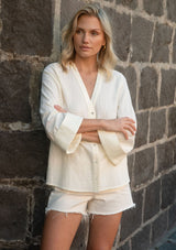 [Color: Eggshell] A front facing image of a blonde model outside wearing a pale yellow blouse with a v-neckline, button front, and wide long sleeves. 