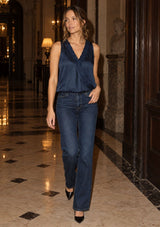 [Color: Midnight] A woman walks down a grand, elegant hallway wearing a dark navy blue satin sleeveless top and dark blue straight-leg jeans.