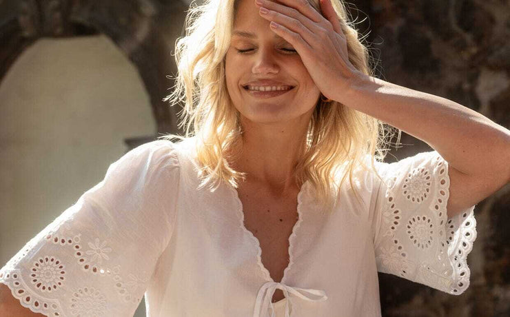 Woman wearing a white blouse with intricate patterns, standing outdoors.