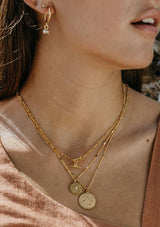 [Zodiac Sign: Pisces] Close-up of a person wearing gold zodiac sign necklace with a neutral background