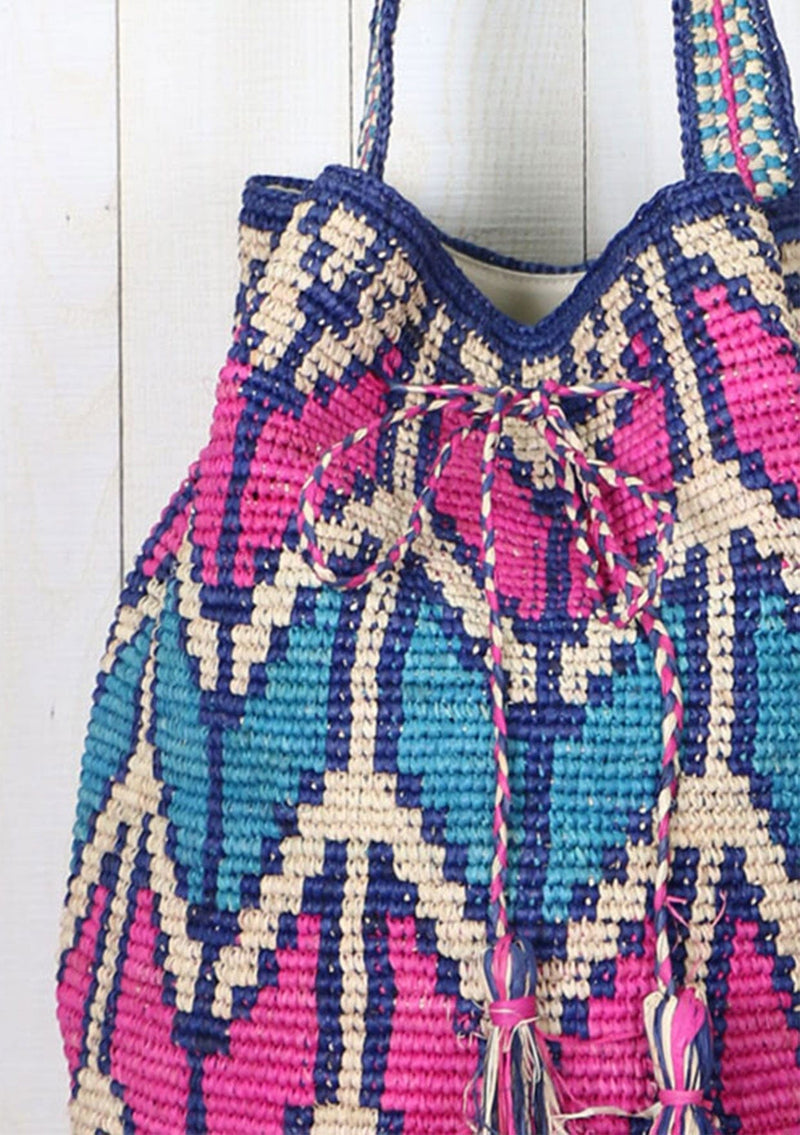 [Color: Hot Pink/Turquoise] A bohemian bucket bag with pink and blue chevron stripe details, made from raffia. With a thick shoulder strap, a drawstring closure, and oversized tassel details. 