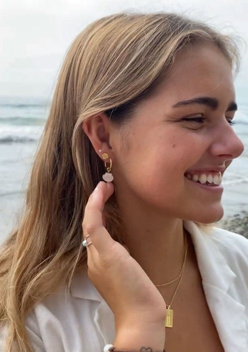 [Color: Gold] A delicate hoop earring with a shell shaped charm crafted from mother of pearl. The hoop is hypoallergenic, made with fourteen karat gold plated sterling silver. 