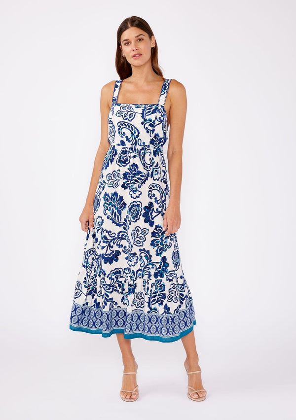 [Color: Vanilla/Navy] Brunette model wearing a blue and white floral tile print midi dress. A stunning dress with a flattering square neckline, sleeveless design, and an open tie back. A cute dress for vacation and warm weather occasions.  
