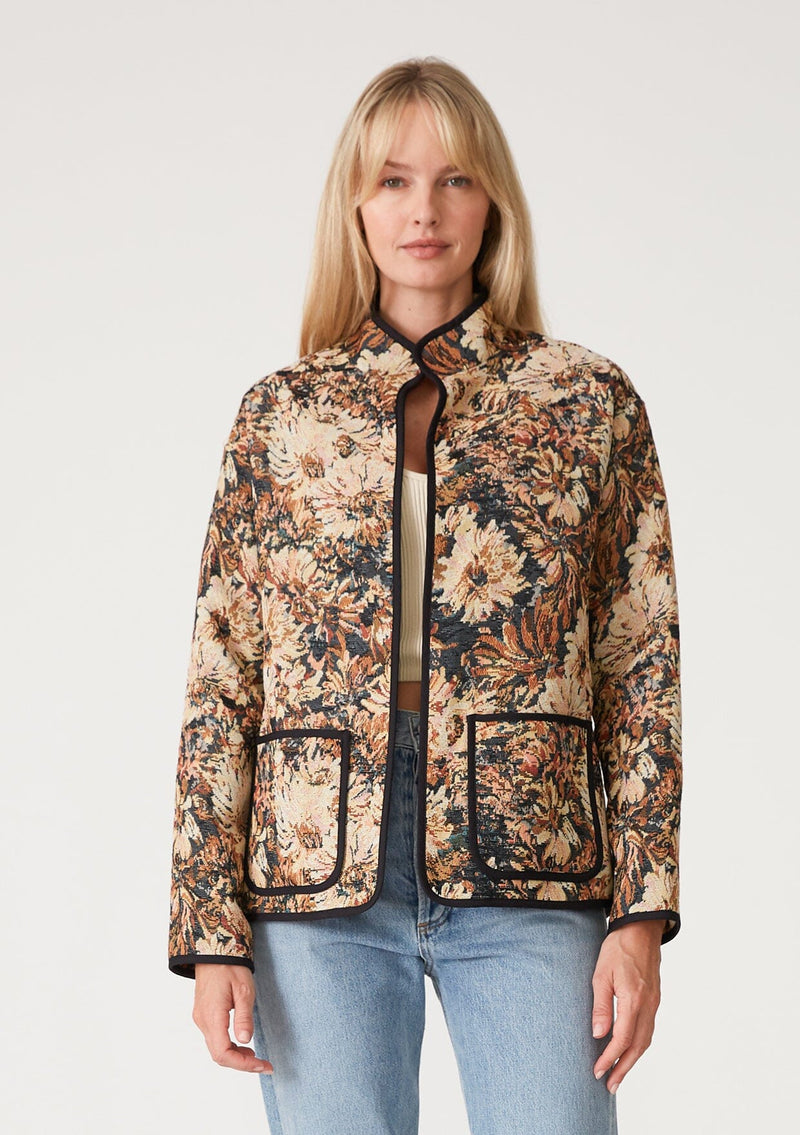 [Color: Black/Natural] A front facing image of a blonde model wearing a bohemian jacket in a black and natural floral tapestry. With long sleeves, a dropped shoulder, an open front, and side patch pockets.