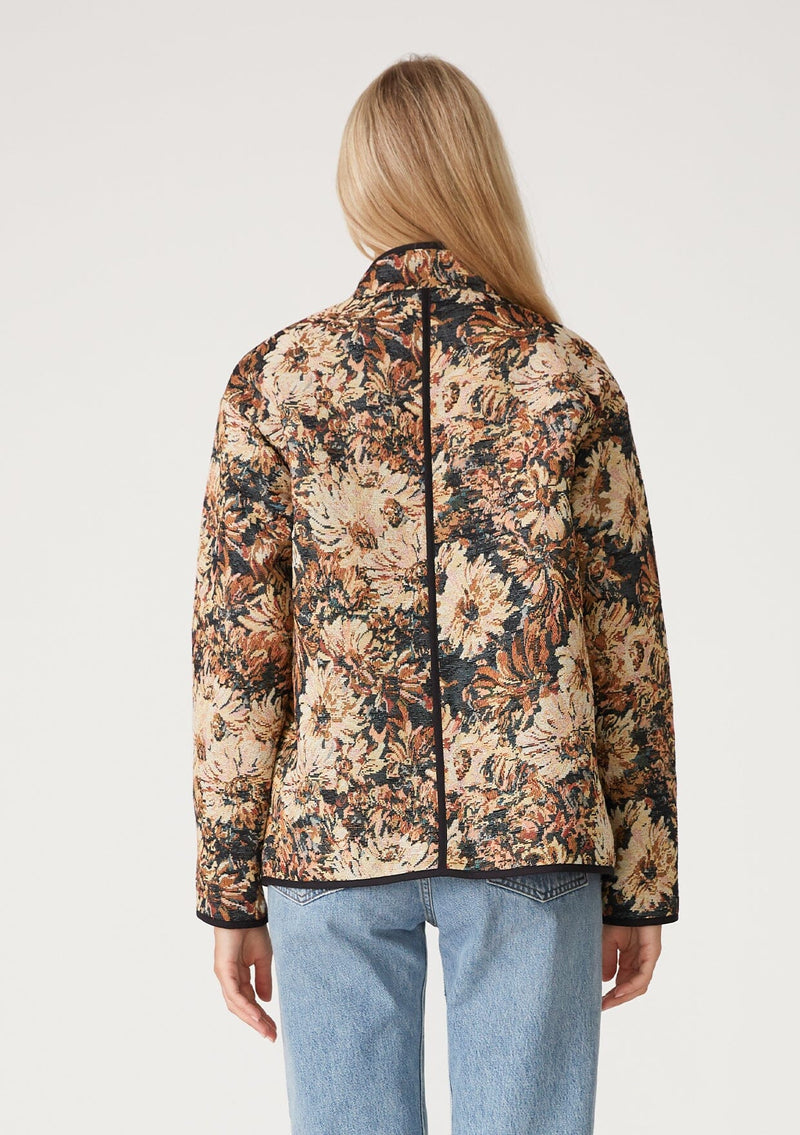 [Color: Black/Natural] A back facing image of a blonde model wearing a bohemian jacket in a black and natural floral tapestry. With long sleeves, a dropped shoulder, an open front, and side patch pockets.
