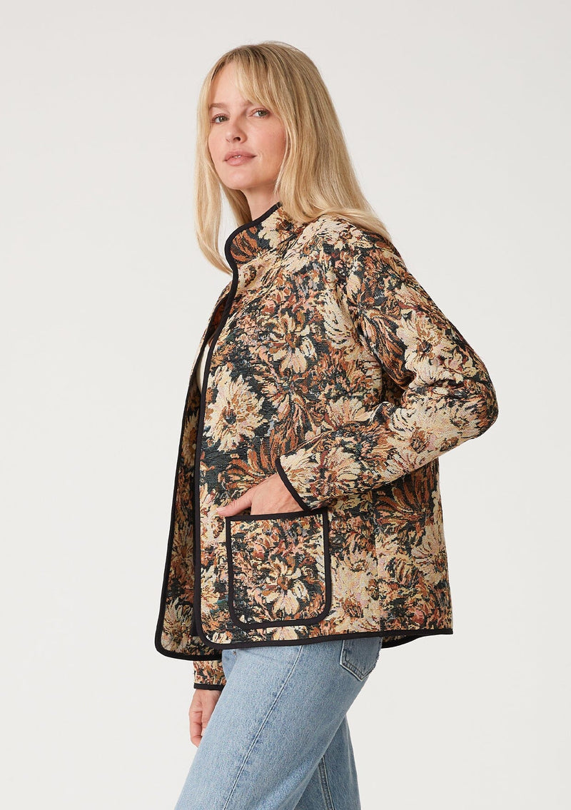 [Color: Black/Natural] A side facing image of a blonde model wearing a bohemian jacket in a black and natural floral tapestry. With long sleeves, a dropped shoulder, an open front, and side patch pockets.