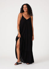 [Color: Black] A front facing image of a brunette model wearing a simple flowy sleeveless maxi tank dress in a black crinkle rayon. With a v neckline in front and back, adjustable spaghetti straps, and a tiered skirt.