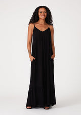 [Color: Black] A front facing image of a brunette model wearing a simple flowy sleeveless maxi tank dress in a black crinkle rayon. With a v neckline in front and back, adjustable spaghetti straps, and a tiered skirt.