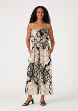 [Color: Black/Khaki] A front facing image of a brunette model wearing a sleeveless jumpsuit in a black and beige bohemian print. With adjustable spaghetti straps, a scoop neckline, side pockets, a long wide leg, and a beaded braided belt. 