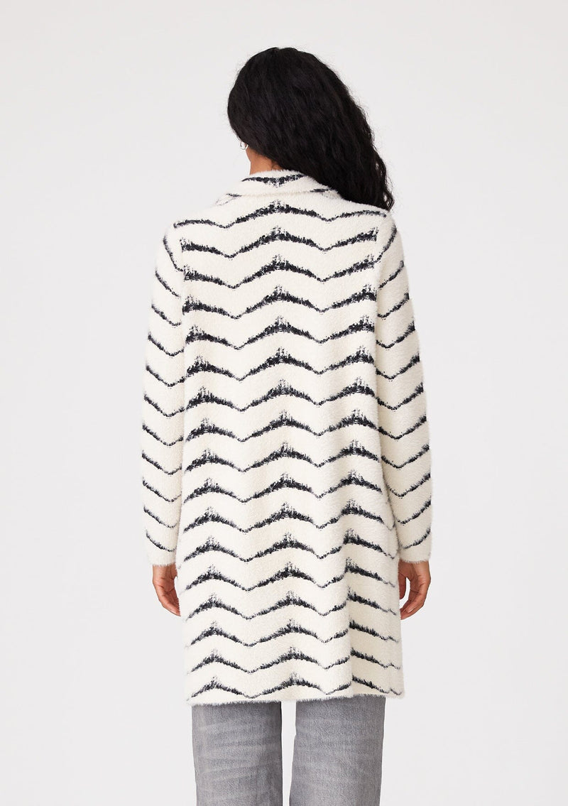 [Color: Cream/Black] A back facing image of a brunette model wearing a soft and fuzzy sweater coat in a white and black chevron design. With a snap button front, side pockets, and a classic notched lapel.