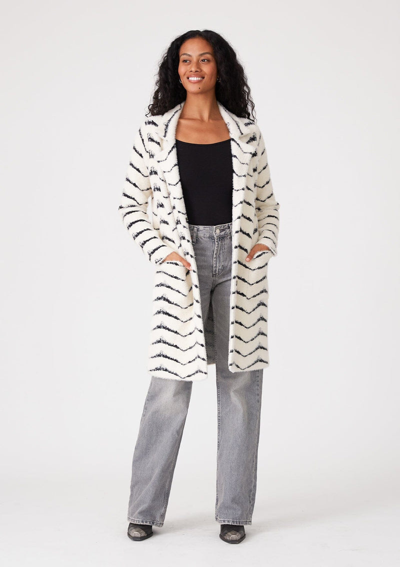 [Color: Cream/Black] A front facing image of a brunette model wearing a soft and fuzzy sweater coat in a white and black chevron design. With a snap button front, side pockets, and a classic notched lapel.
