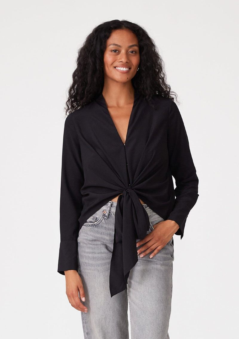 [Color: Black] A front facing image of a brunette model wearing a black button front blouse with a tie waist detail. With a button front, a deep v neckline, long sleeves, and long wrist cuffs with a button closure. 