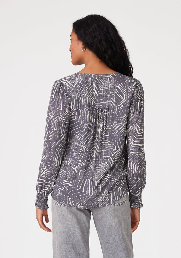 [Color: Grey/Cream] A back facing image of a brunette model wearing a bohemian fall blouse in an abstract grey print. With long sleeves, a round neckline, and a self covered button front. 