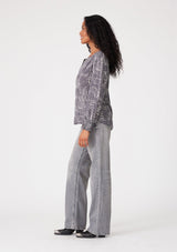 [Color: Grey/Cream] A side facing image of a brunette model wearing a bohemian fall blouse in an abstract grey print. With long sleeves, a round neckline, and a self covered button front. 