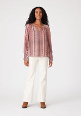 [Color: Cinnamon/Coral] A full body front facing image of a brunette model wearing a bohemian fall blouse in a pink print. With long sleeves, a loop button front, a v neckline, and tapered sleeves. 