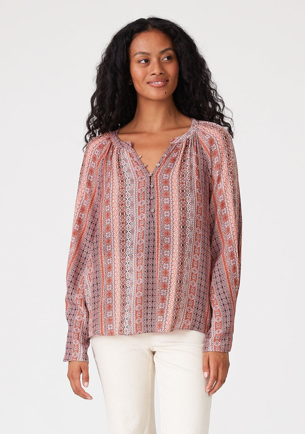 [Color: Cinnamon/Coral] A front facing image of a brunette model wearing a bohemian fall blouse in a pink print. With long sleeves, a loop button front, a v neckline, and tapered sleeves. 