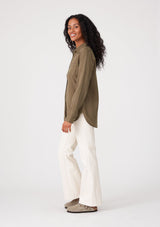 [Color: Military] A side facing image of a brunette model wearing a relaxed fit olive green shirt. With long sleeves, a collared neckline, a button front, and front patch pockets. 