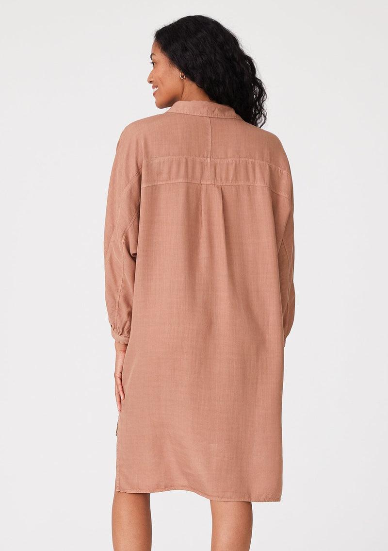 [Color: Clay] A back facing image of a brunette model wearing a pink relaxed fit shirt dress. With long sleeves, a button front, a high low hemline, a collared neckline, and front flap pockets. 