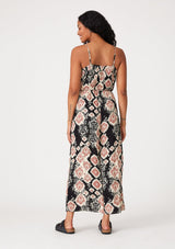 [Color: Black/Dusty Rose] A back facing image of a brunette model wearing a sleeveless jumpsuit in a black and pink bohemian print. With adjustable spaghetti straps, a scoop neckline, side pockets, a long wide leg, and a beaded braided belt. 