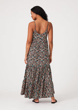[Color: Black/Teal] A back facing image of a brunette model wearing a bohemian maxi dress in a black and teal floral print. With adjustable spaghetti straps, a scalloped trim v neckline with contrast thread details, a tiered flowy silhouette, side pockets, and an empire waist.