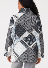 [Color: Natural/Blue] A back facing image of a brunette model wearing a blue and white patchwork print quilted jacket. With long sleeves, a shawl collar, side pockets, and a tie waist belt. 