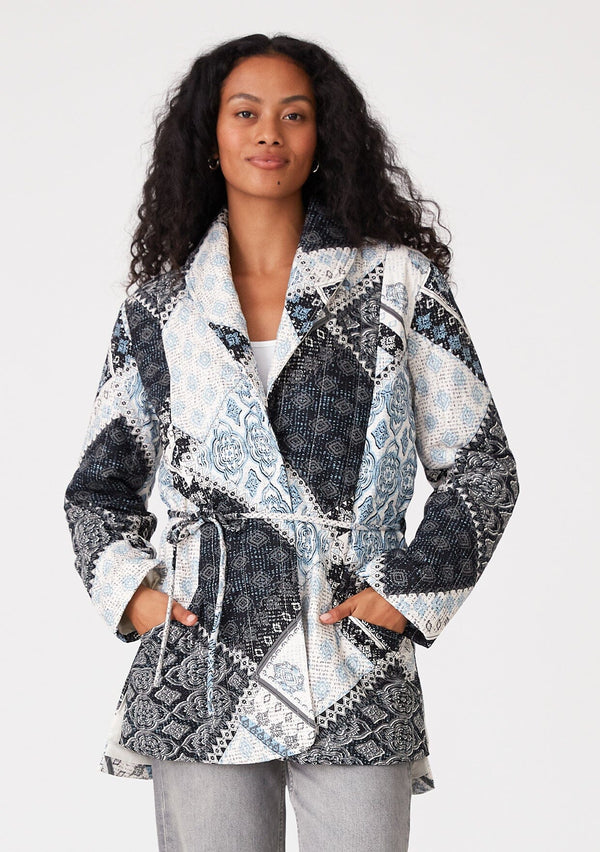 [Color: Natural/Blue] A front facing image of a brunette model wearing a blue and white patchwork print quilted jacket. With long sleeves, a shawl collar, side pockets, and a tie waist belt. 