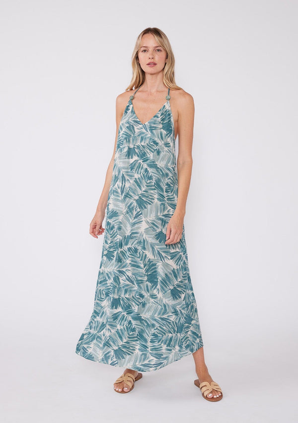 [Color: Natural/Green] A front facing image of a blonde model wearing a sleeveless summer maxi dress in a tropical green palm leaf print. With a v neckline, spaghetti straps with bead accents, a strappy back with adjustable tie, and a flowy silhouette. 