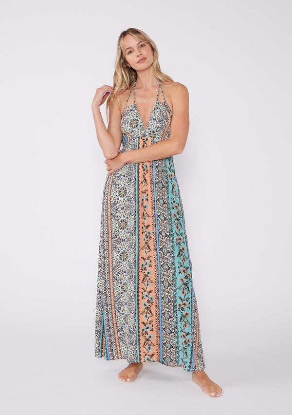 [Color: Natural/Tangerine] A front facing image of a blonde model wearing a sleeveless summer maxi dress in a bohemian mixed floral print, with gold metallic thread details. With a halter v neckline, an empire waist, and a strappy back with adjustable ties. 
