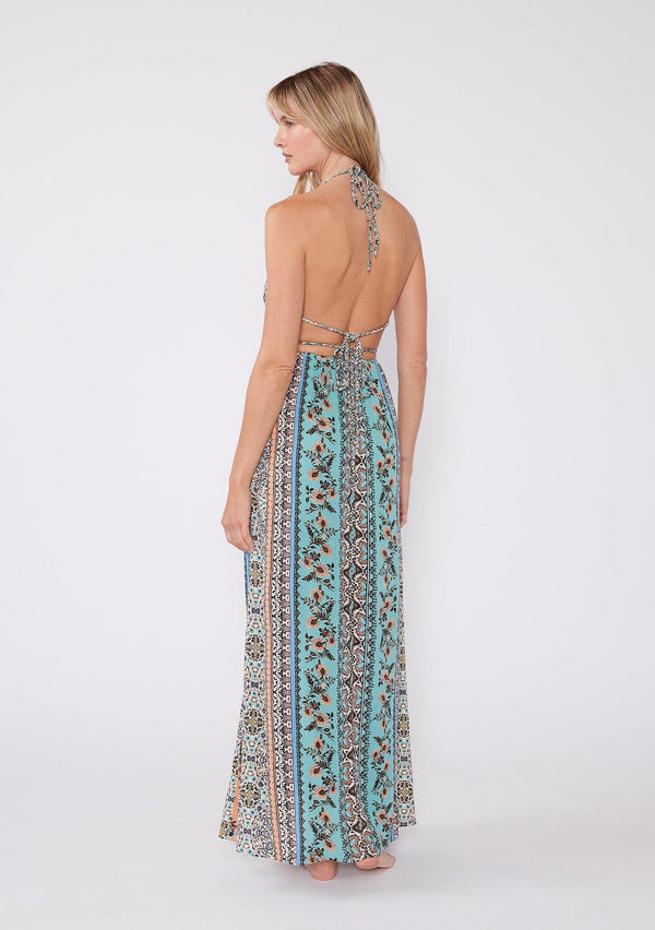 [Color: Natural/Tangerine] A back facing image of a blonde model wearing a sleeveless summer maxi dress in a bohemian mixed floral print, with gold metallic thread details. With a halter v neckline, an empire waist, and a strappy back with adjustable ties. 
