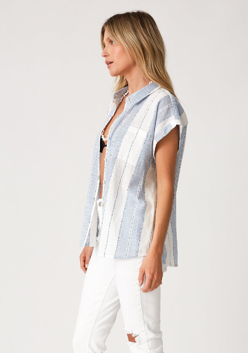 [Color: White/Blue] A side facing image of a blonde model wearing a white and blue striped shirt with short cuffed sleeves, a button front, a classic collared neckline, and a front patch pocket.