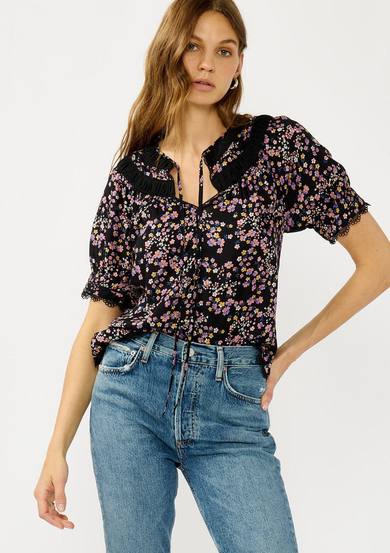 [Color: Black/Pink] A front facing image of a black and pink floral print top with puff sleeves, a split v-neckline with ties, shirred details, and lace trims. A day to night versatile top for the fall season. 