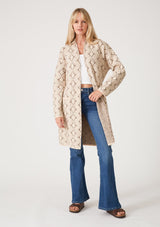[Color: Natural/Taupe] A full body front facing image of a blonde model wearing a soft mid length cardigan sweater coat in an ivory diamond jacquard. With long sleeves, side pockets, and a belted tie waist.