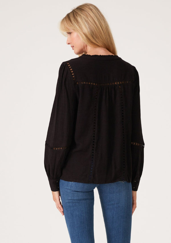 [Color: Black] A back facing image of a blonde model wearing a black linen blend bohemian blouse. With voluminous long sleeves, delicate crochet trim, and a self covered button front.