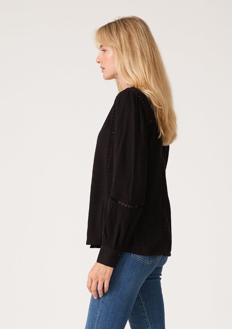 [Color: Black] A side facing image of a blonde model wearing a black linen blend bohemian blouse. With voluminous long sleeves, delicate crochet trim, and a self covered button front.